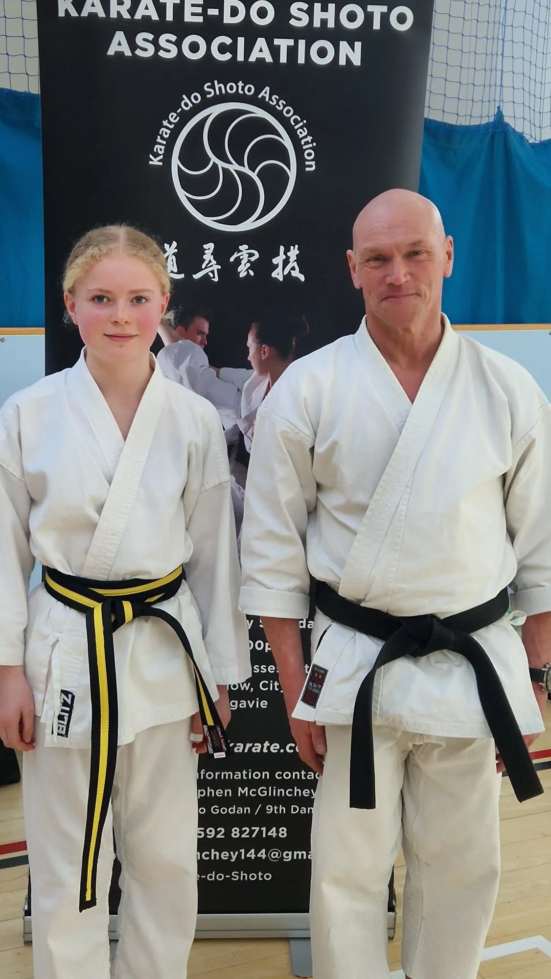 Laila and Wilf in their gis in front of the Karate-do Shoto Association banner
