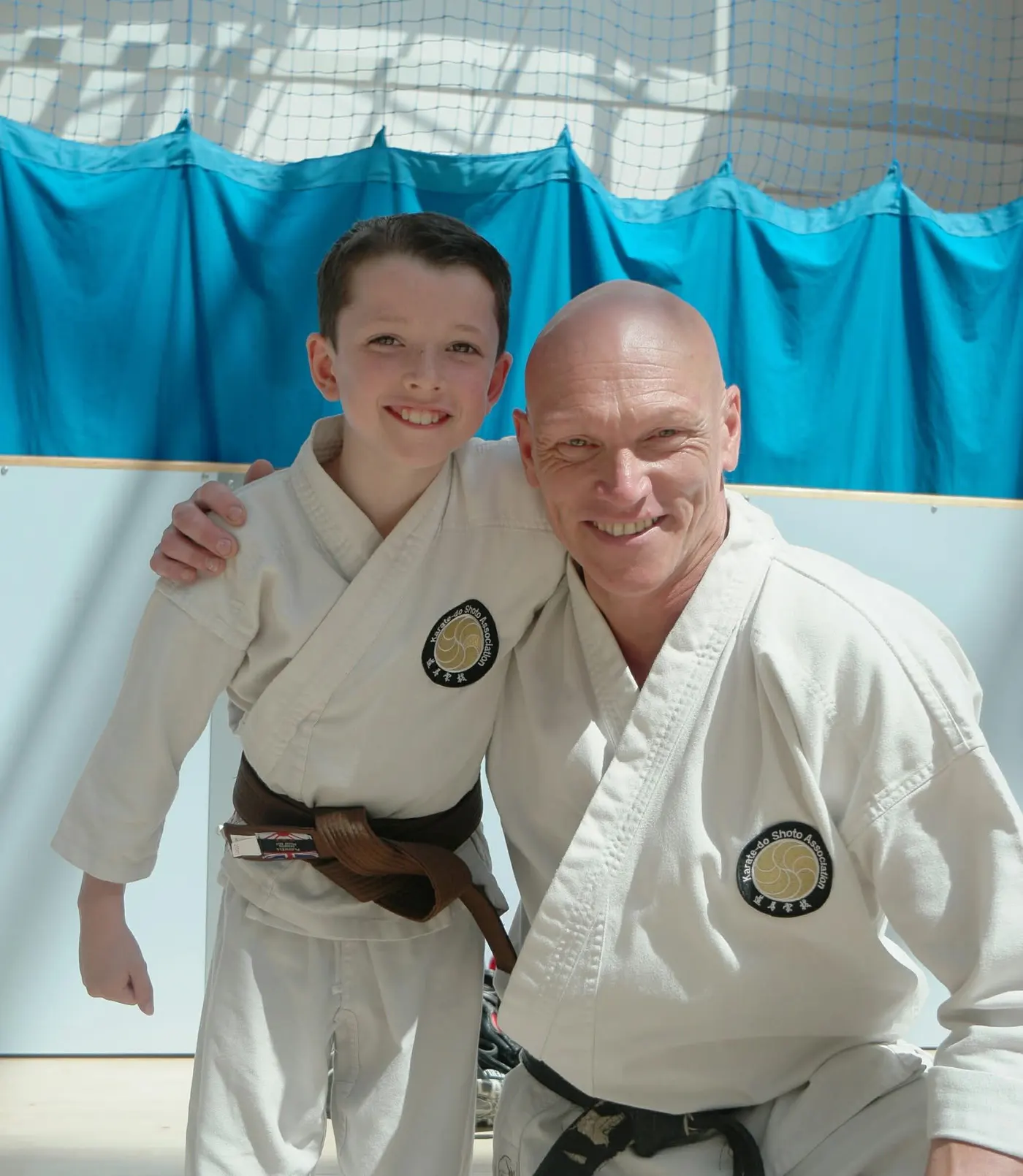 A junior member with a brown belt standing beside his instructor