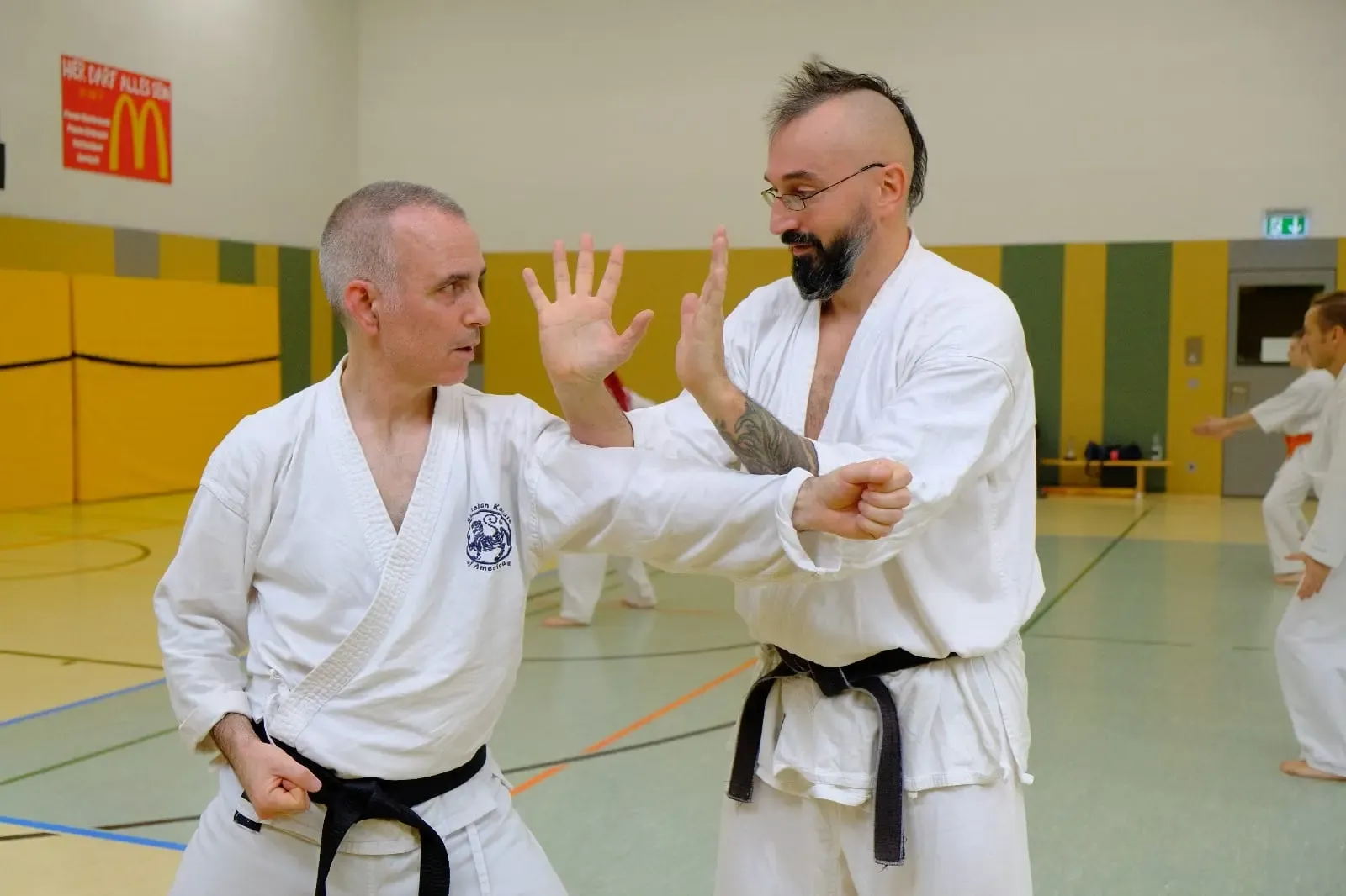 Two senior members practising a block and strike in a school sports hall