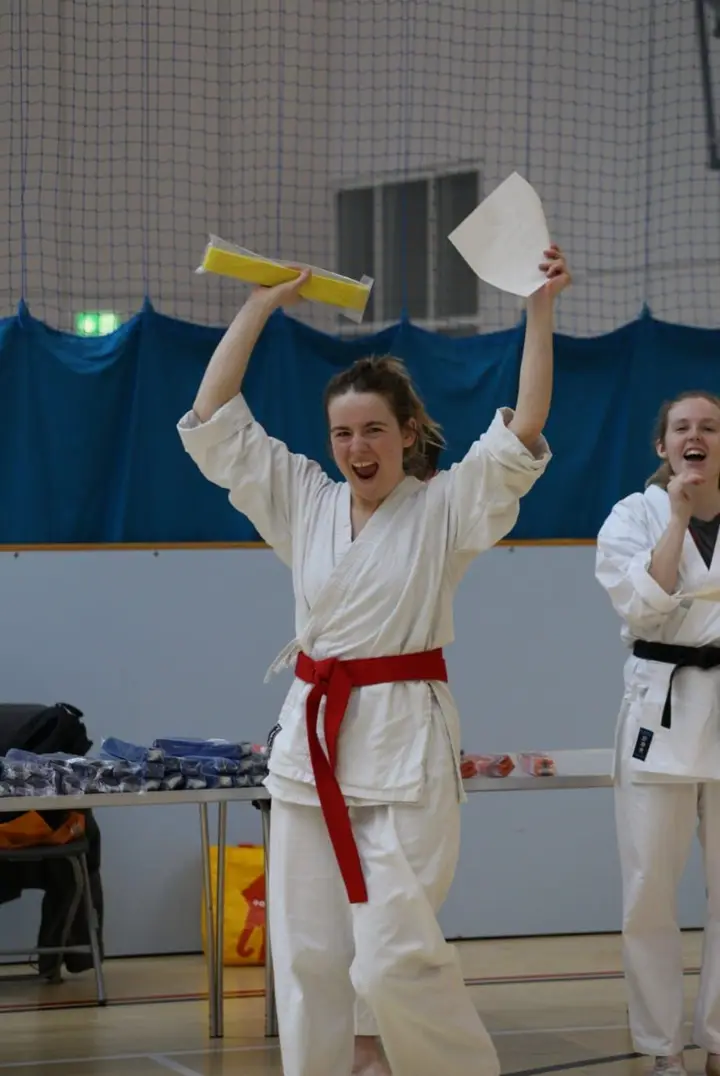A member with a new red belt celebrating with arms raised