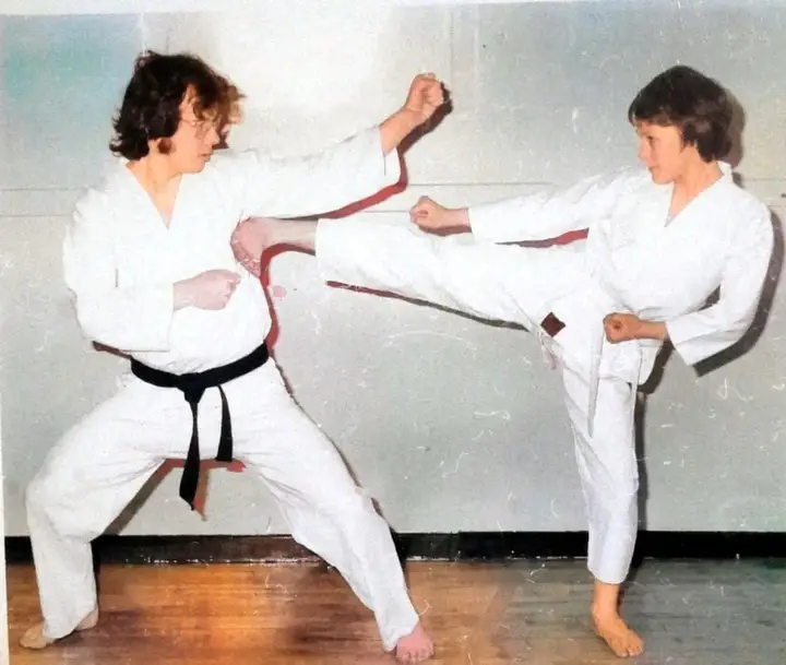 Two seniors practising a kick and block in a hall