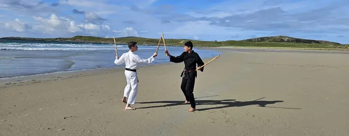 Two members practising with bo staffs on an Islay beach