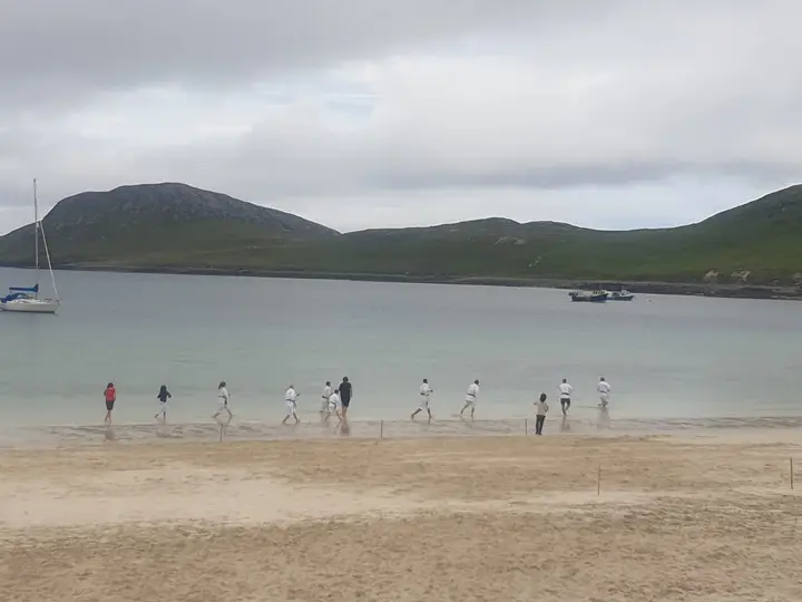 A class training on a wide beach below green hills