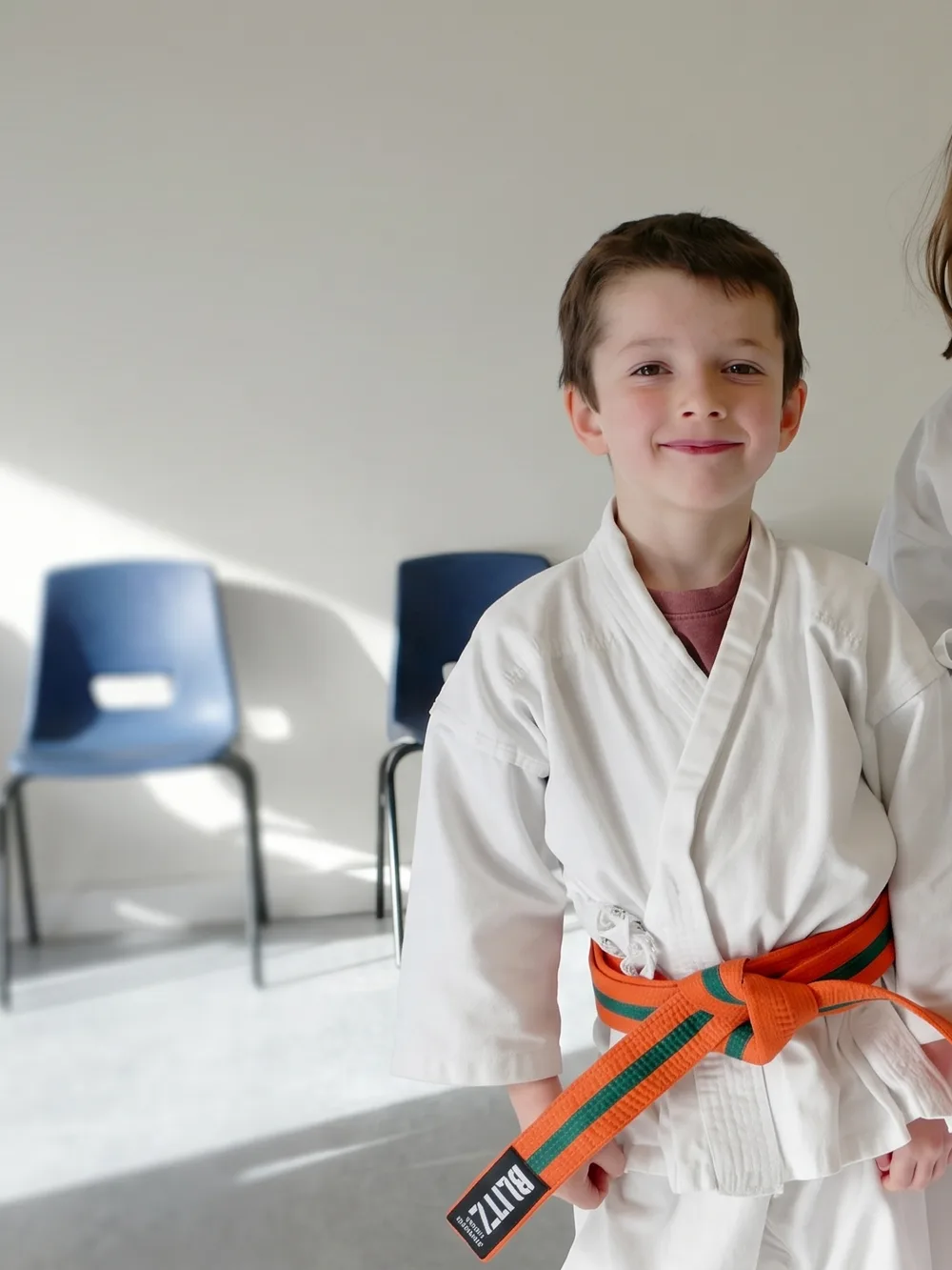 Two young members in white gis, one with an orange belt and one with a purple belt